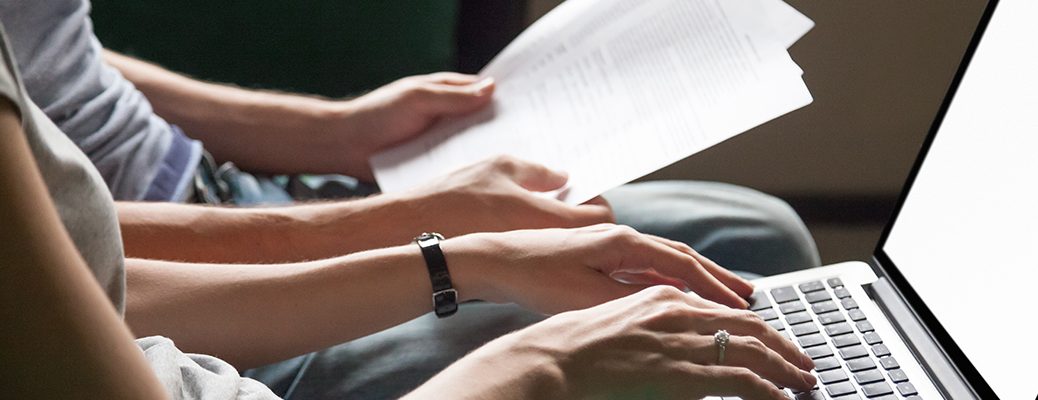 Two individuals review documents while applying online using a laptop, representing quick loan access. Get instant personal loans online with IndusInd Bank.