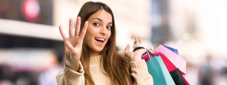 A woman enjoying her shopping spree and gesturing four to refer four types of instant credit cards by IndusInd Bank.