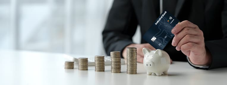 Man inserting IndusInd Bank RuPay credit card into piggy bank, symbolizing savings and rewards.