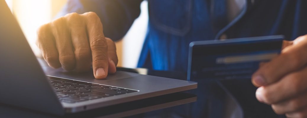 Person using laptop holding a credit card. Learn how to apply online for a credit card and choose IndusInd bank for easy application.