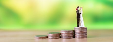 A bride and groom figurine atop stacked coins shows growing wedding costs. Explore Personal Loan for Marriage from IndusInd Bank for your wedding budget.