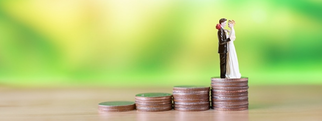 A bride and groom figurine atop stacked coins shows growing wedding costs. Explore Personal Loan for Marriage from IndusInd Bank for your wedding budget.