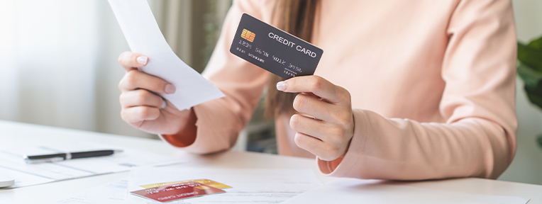Person holding a credit card and bill, showing how to pay one credit card bill using another credit card with IndusInd Bank services.
