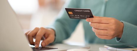 Person holding credit card at laptop, highlighting strategies to avoid credit card delinquency like automating payments.