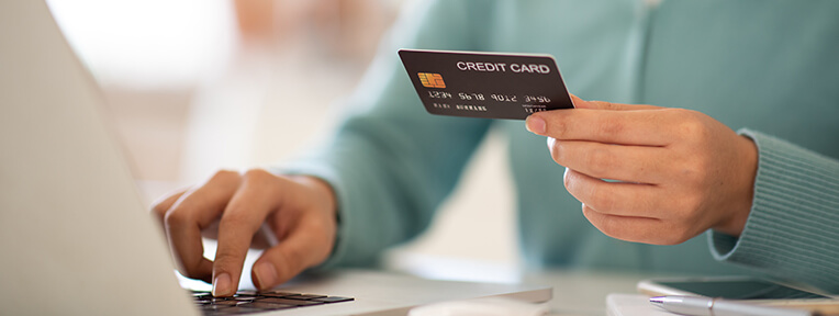 Person holding credit card at laptop, highlighting strategies to avoid credit card delinquency like automating payments.