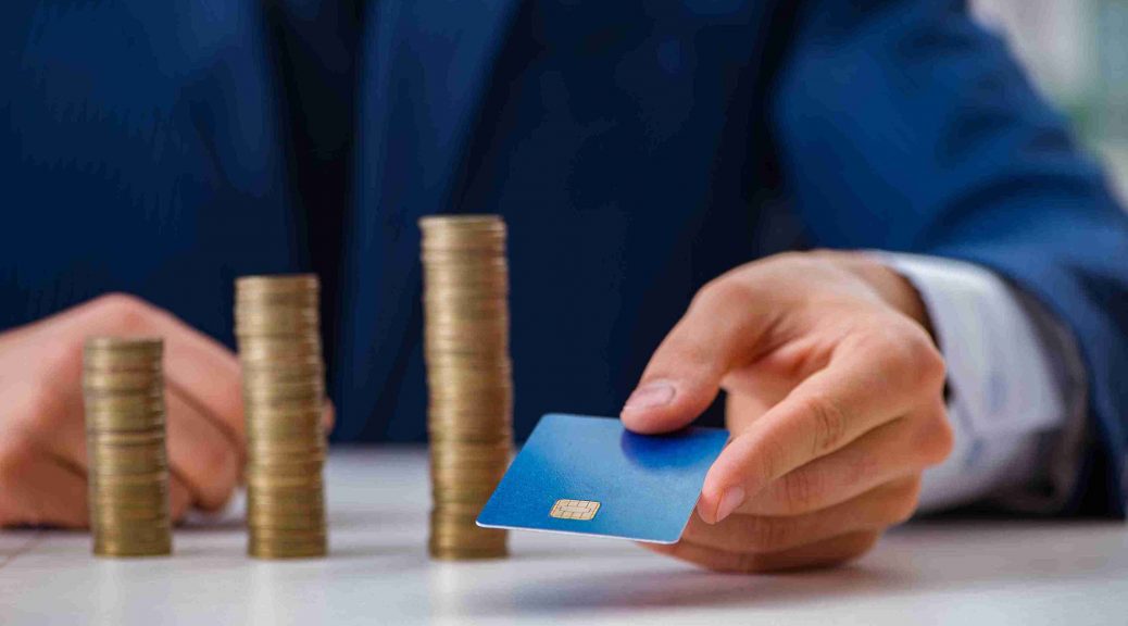 Hand holding a card beside stacks of coins, explaining Forex card function. Discover IndusInd Bank Forex Cards for easy currency management