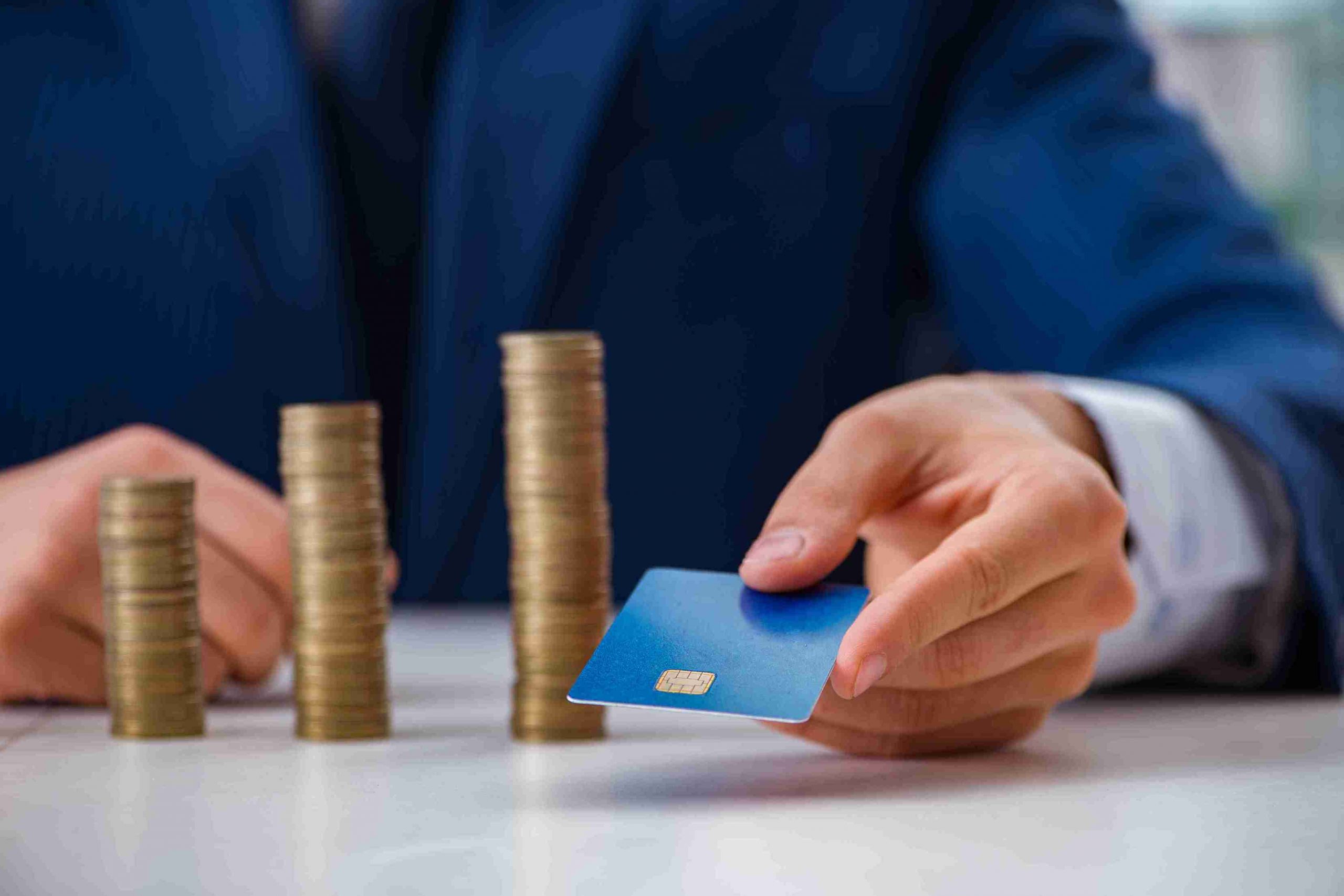 Hand holding a card beside stacks of coins, explaining Forex card function. Discover IndusInd Bank Forex Cards for easy currency management