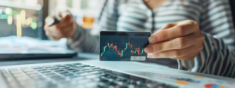 Person holding card with currency graph at a laptop. Debunk Forex card myths and discover the truth with IndusInd Bank Forex Card benefits.