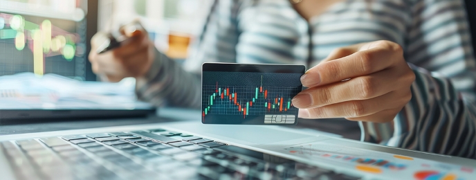 Person holding card with currency graph at a laptop. Debunk Forex card myths and discover the truth with IndusInd Bank Forex Card benefits.