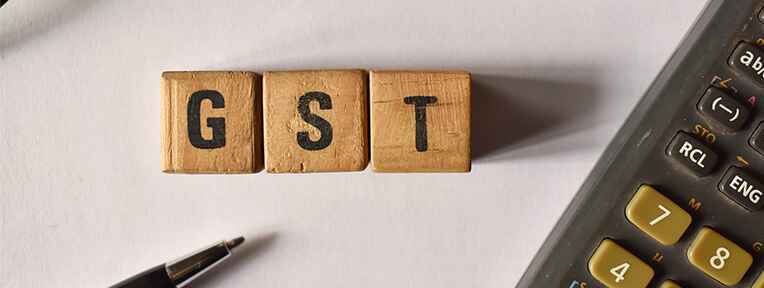 Wooden blocks "GST" with pen, calculator imply IndusInd Bank Credit Card's GST interest rate calculations.