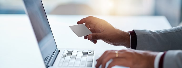 Person holding a credit card at a laptop, illustrating applying for a credit card loan with IndusInd Bank.