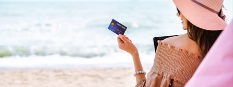 Woman on a beach holding Indus Multicurrency Forex Card, enjoying stress-free travel with global convenience.