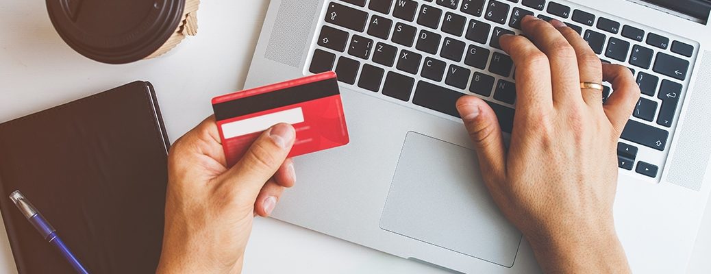 Hands holding a credit card and typing on a laptop, highlighting responsible usage of IndusInd Bank Credit Card.