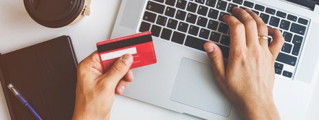 Hands holding a credit card and typing on a laptop, highlighting responsible usage of IndusInd Bank Credit Card.