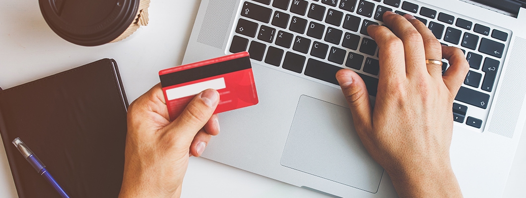 Hands holding a credit card and typing on a laptop, highlighting responsible usage of IndusInd Bank Credit Card.